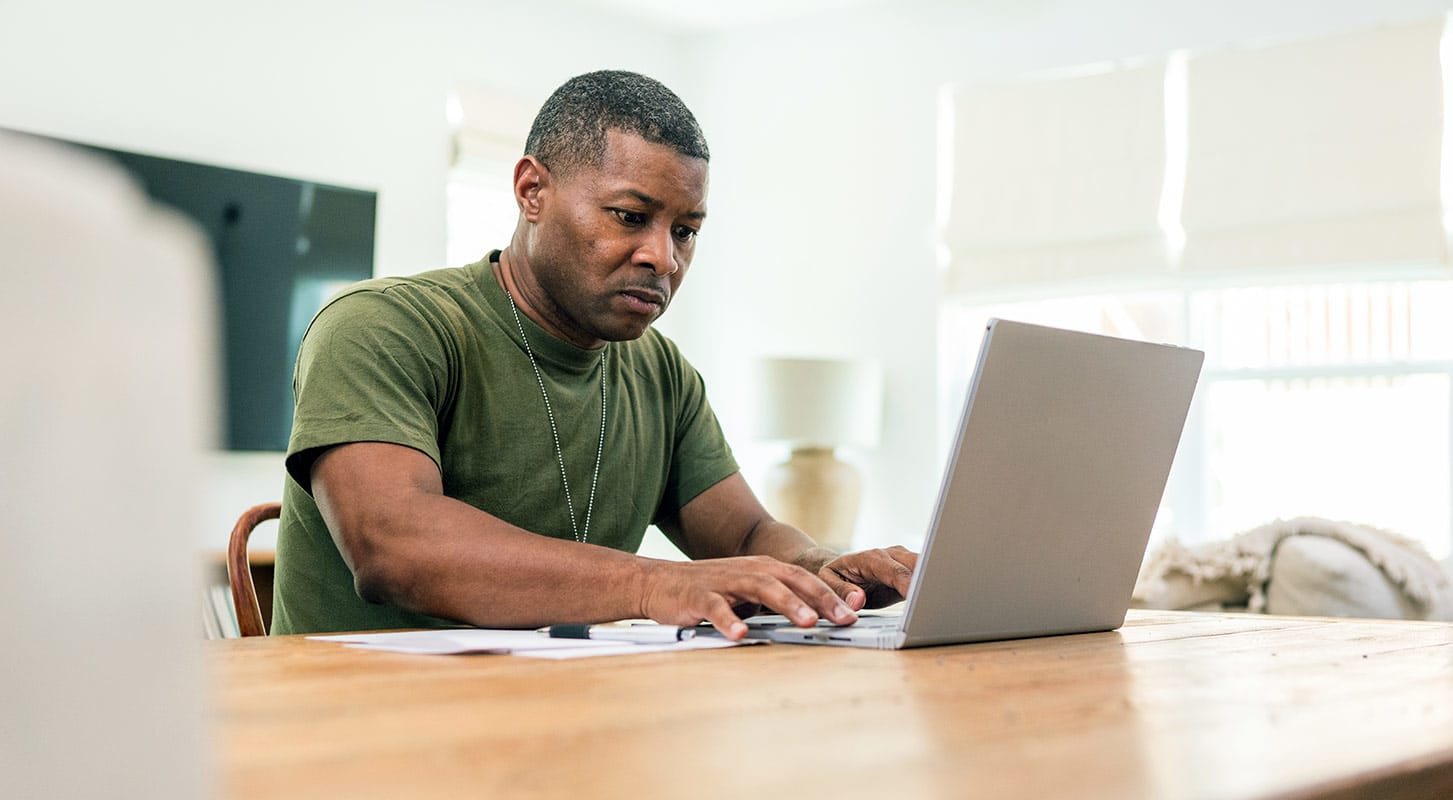 A man sitting at a table, focused on his laptop.